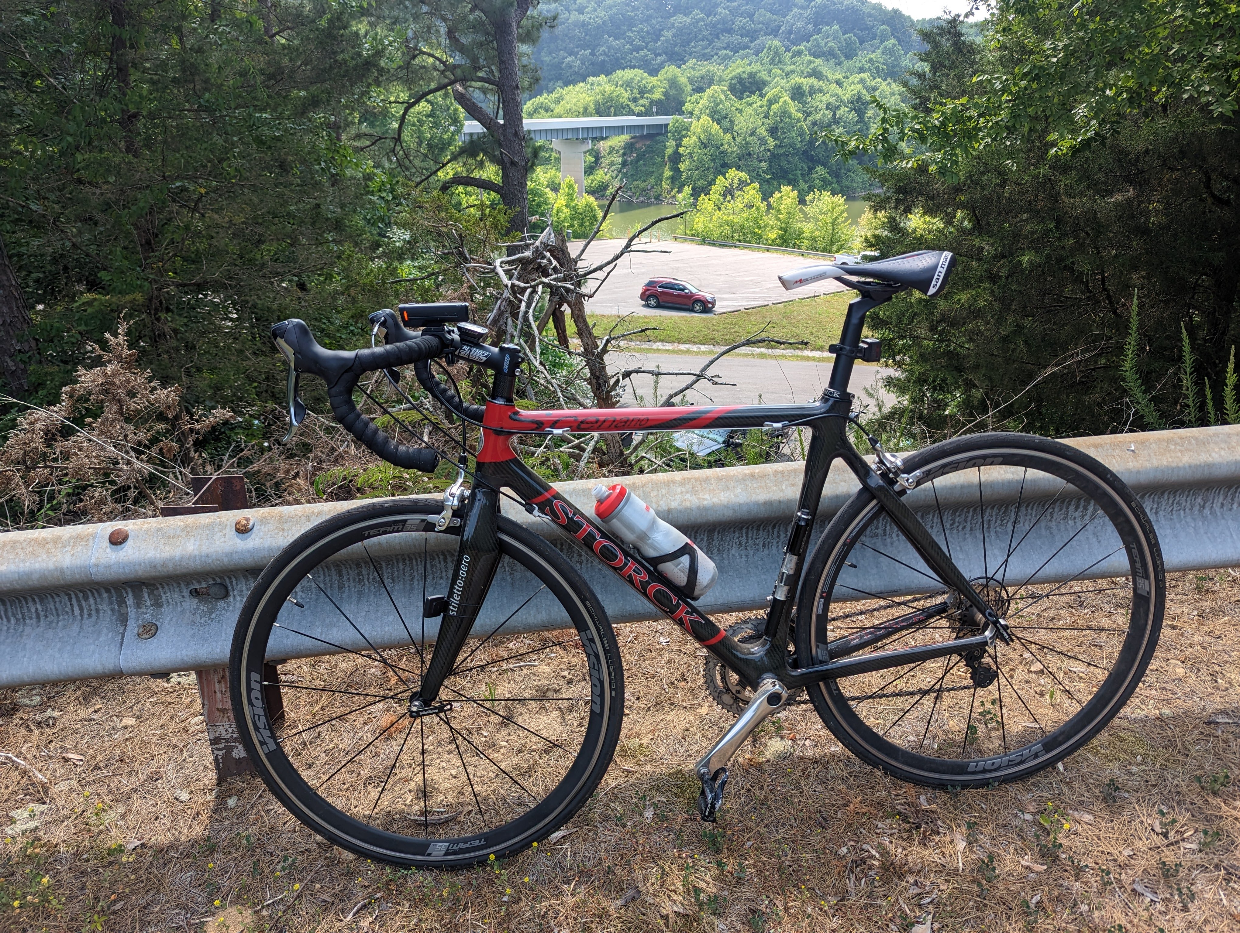 a red and black carbon fiber bike leaning against a guardrail overlooking a boat launch and river
